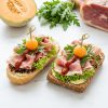 Belegte halbe Brötchen mit Serranoschinken, Melonenkugeln, Rucola und Rotem Pesto von ehab Catering